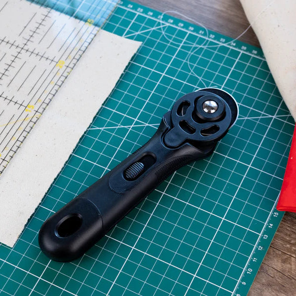 Black rotary cutter on a green cutting mat with fabric and ruler